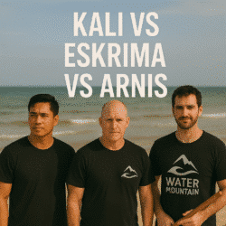 Three martial artists stand on a beach after training, wearing Water Mountain logo t-shirts, under the text "Kali vs Escrima vs Arnis."