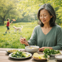 Woman in her late 50s enjoying a fresh spring meal outdoors in a park while a child and dog play in the background.